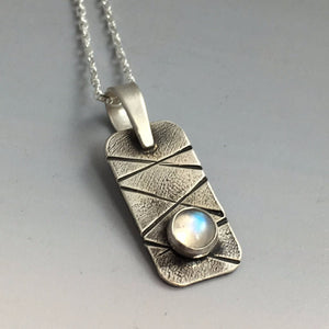 close-up view of one small silver pendant with bezel set moonstone